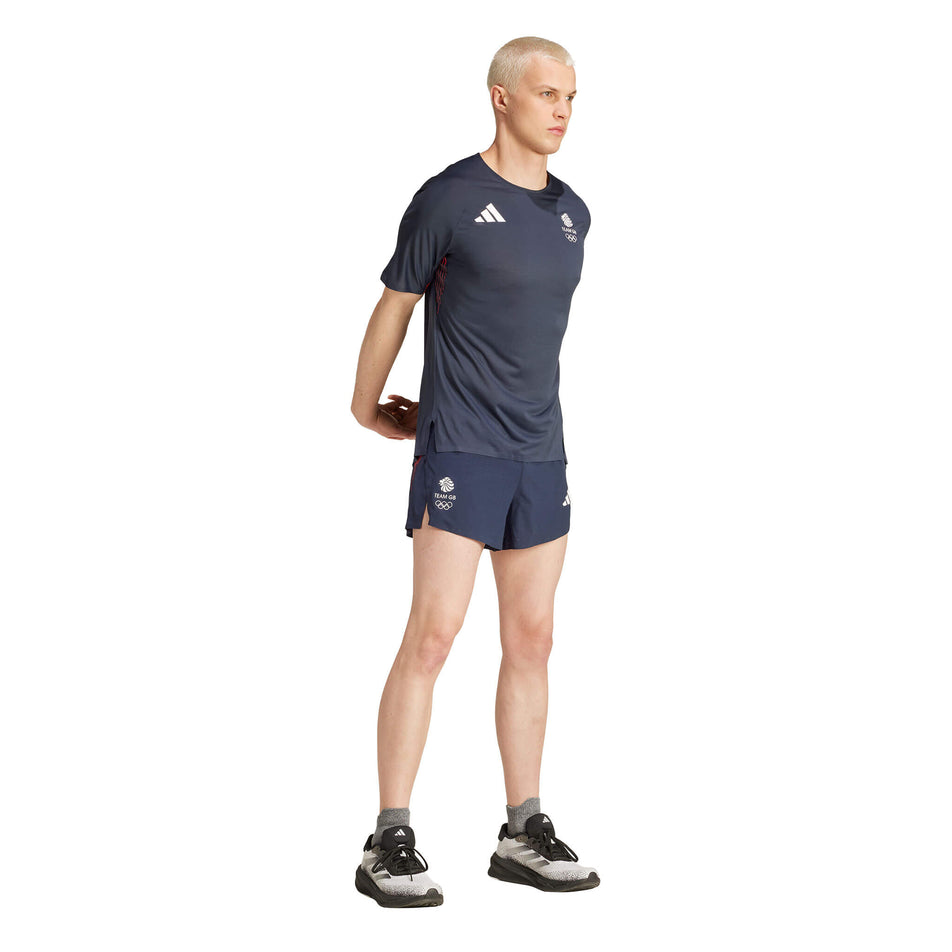 Angled front view of a model wearing an adidas Men's Team GB Adizero Running T-Shirt in the Legend Ink colourway. Model is also wearing adidas shorts, socks and shoes, and is stretching. (8324017553570)