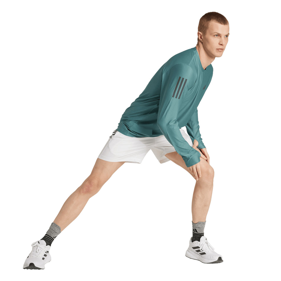 Angled view of a model wearing the adidas Men's Own The Run Base Long Sleeve in the Preloved Teal colourway. (8751018180770)
