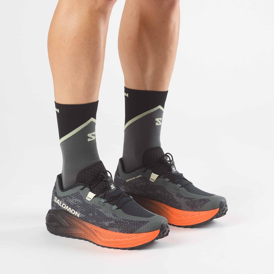 A model wearing a pair of Salomon Men's Aero Glide 4 GRVL Running Shoes in the Urban Chic/Black colourway.