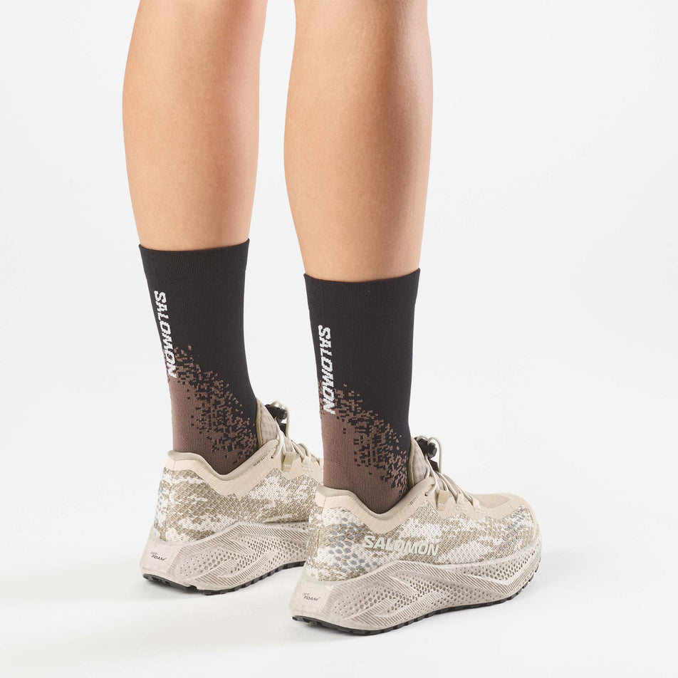 A model wearing a pair of Salomon Women's Aero Glide 4 GRVL Running Shoes in the Tapioca/Desert Tan colourway.