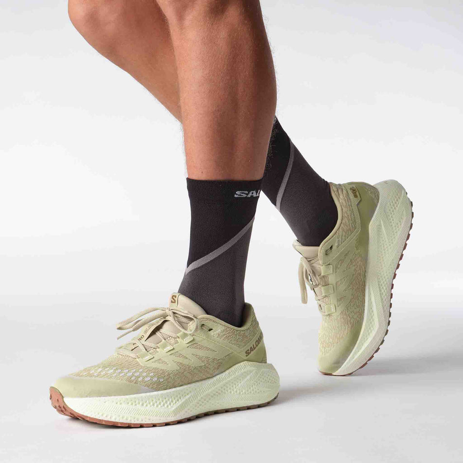 Side view of a model wearing a pair of Salomon Men's Aero Glide 3 GRVL Running Shoes in the Green Haze/Vanilla Ice/Russet colourway. (8644590469282)