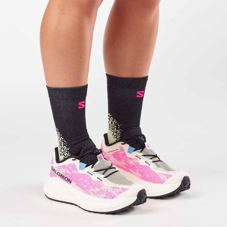 A model wearing a pair of Salomon Women's Aero Glide 4 GRVL Running Shoes in the Vanilla Ice/Knockout Pink/Black colourway.