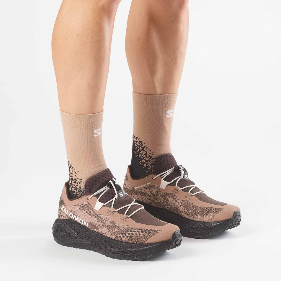 A model wearing a pair of Salomon Men's Aero Glide 4 GRVL Running Shoes in the Burro/Black colourway.