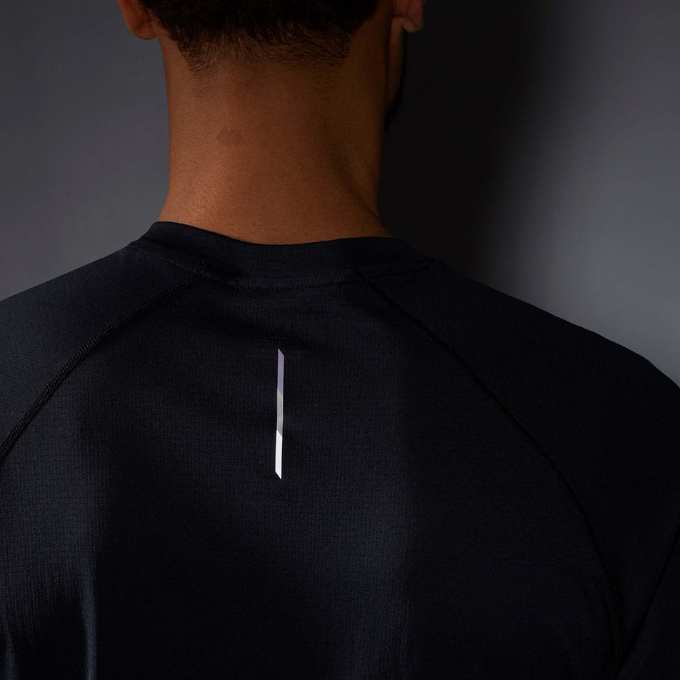 Close-up view of the upper-back section of a Salomon Men's Cross Run Long Sleeve T-Shirt in the Deep Black colourway. Worn by a model in low light conditions to show the reflective strip on the fabric. (8008540324002)