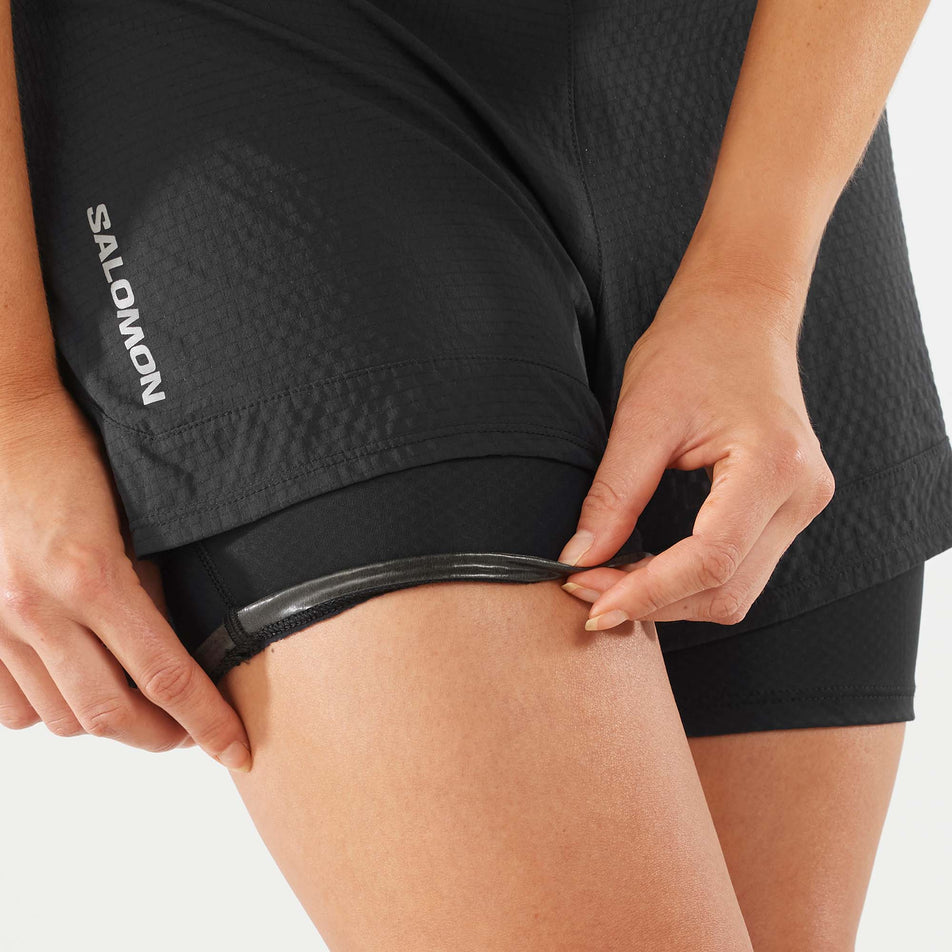 Close-up front view of a model wearing a pair of Salomon Women's Sense 2in1 Shorts in the Deep Black colourway, showing the enhanced grip on the inside of the lower part of the inner liner. (8000776437922)