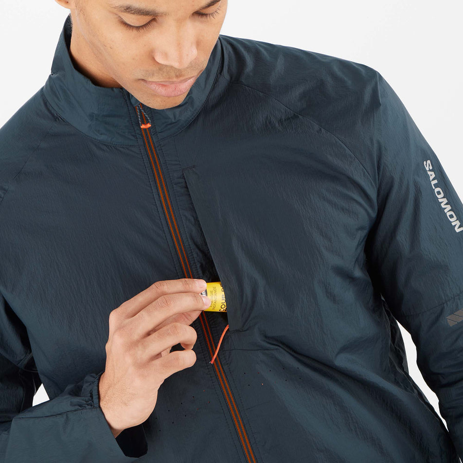 A model demonstrating that an energy gel can be stored in the chest pocket of a Salomon Men's Sense Flow Jacket in the Carbon/Carbon colourway (8071109771426)