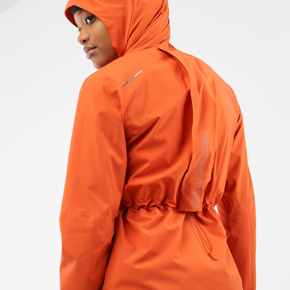 Back view of a model wearing a Salomon Women's Bonatti Trail Jacket in the Burnt Ochre colourway, with the hood up. (8000727351458)