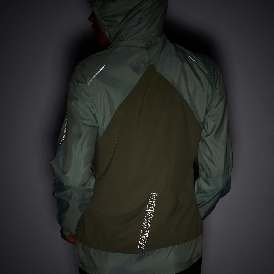 Front view of a model wearing a Salomon Women's Bonatti Cross Wind Jacket in the Lily Pad/Deep Lichen Green colourway. The jacket's reflective details are visible. (7999055462562)
