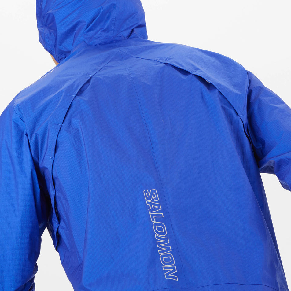 Close-up back view of a model wearing a Salomon Men's Bonatti Waterproof Jacket in the Surf The Web colourway. The back vents can be seen in the image. (8008537833634)