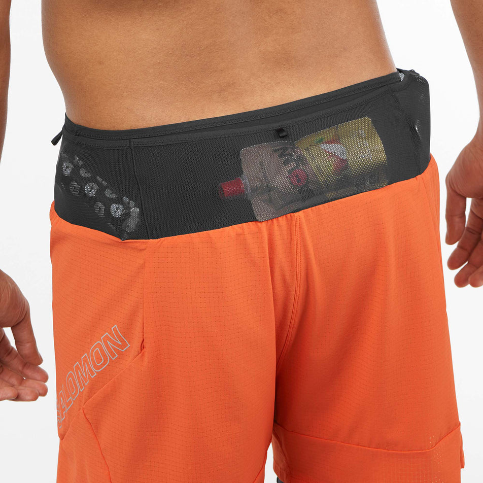 Close-up back view of a model wearing a pair of Salomon Men's Sense Aero 2in1 Shorts in the Burnt Ochre colourway, demonstrating that nutrition can be stored in the mesh pockets on the waistband. (8008583315618)