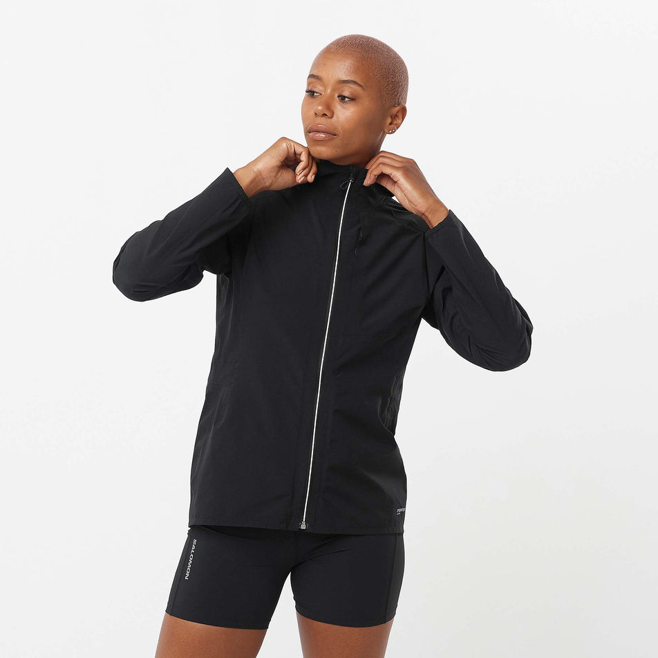 Front view of a model wearing a Salomon Women's Bonatti Trail Jacket in the Deep Black colourway. Model is also wearing Salomon shorts.  (8157861019810)