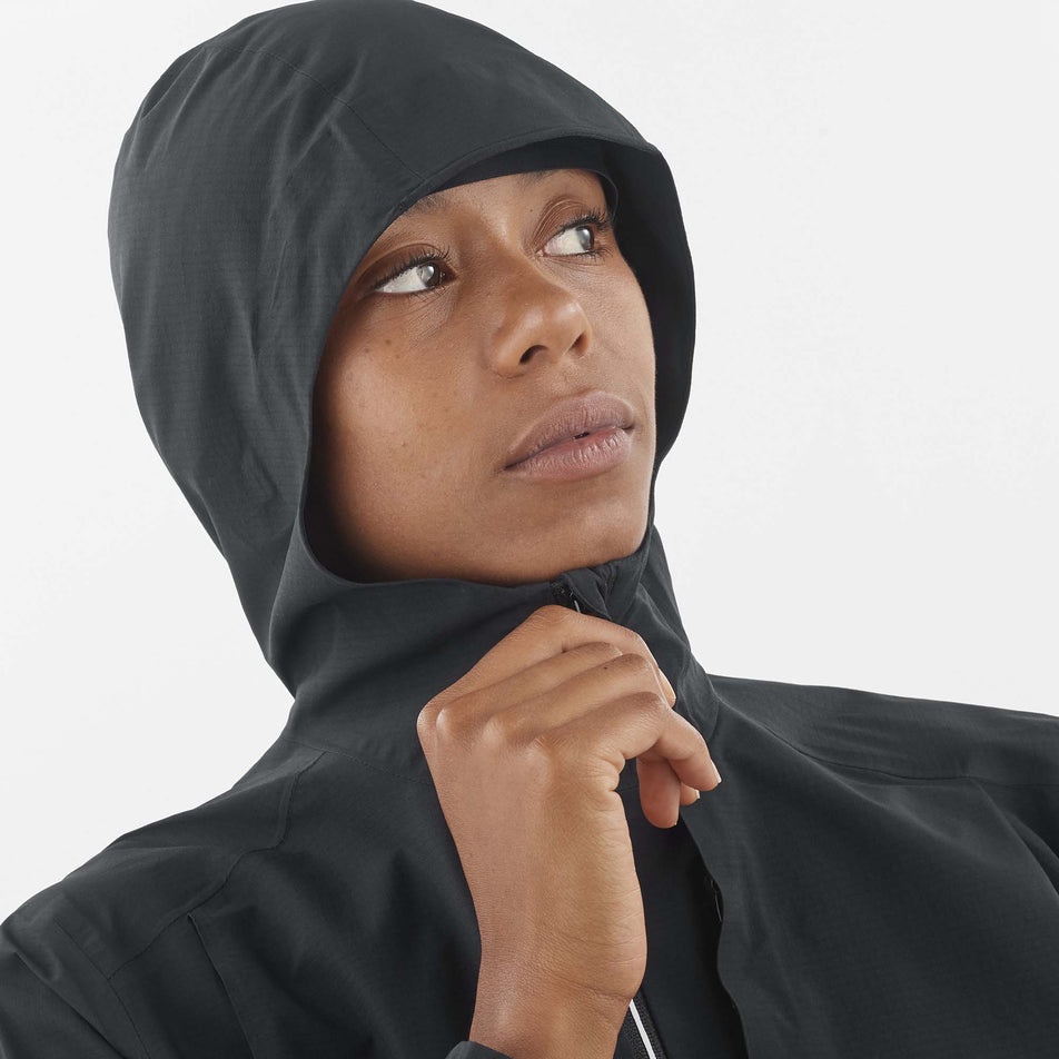 Close-up front view of a model wearing a Salomon Women's Bonatti Trail Jacket in the Deep Black colourway. Model has the jacket's hood up. (8157861019810)