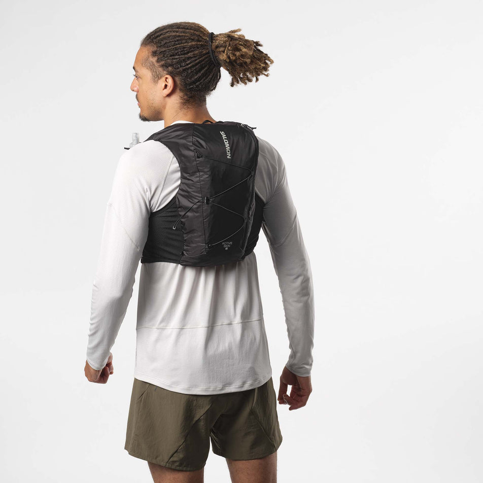 Back view of a model wearing a Salomon Unisex Active Skin 8 Running Vest with flasks. Black/Metal colourway. Model is also wearing a running top and shorts. (8151560880290)