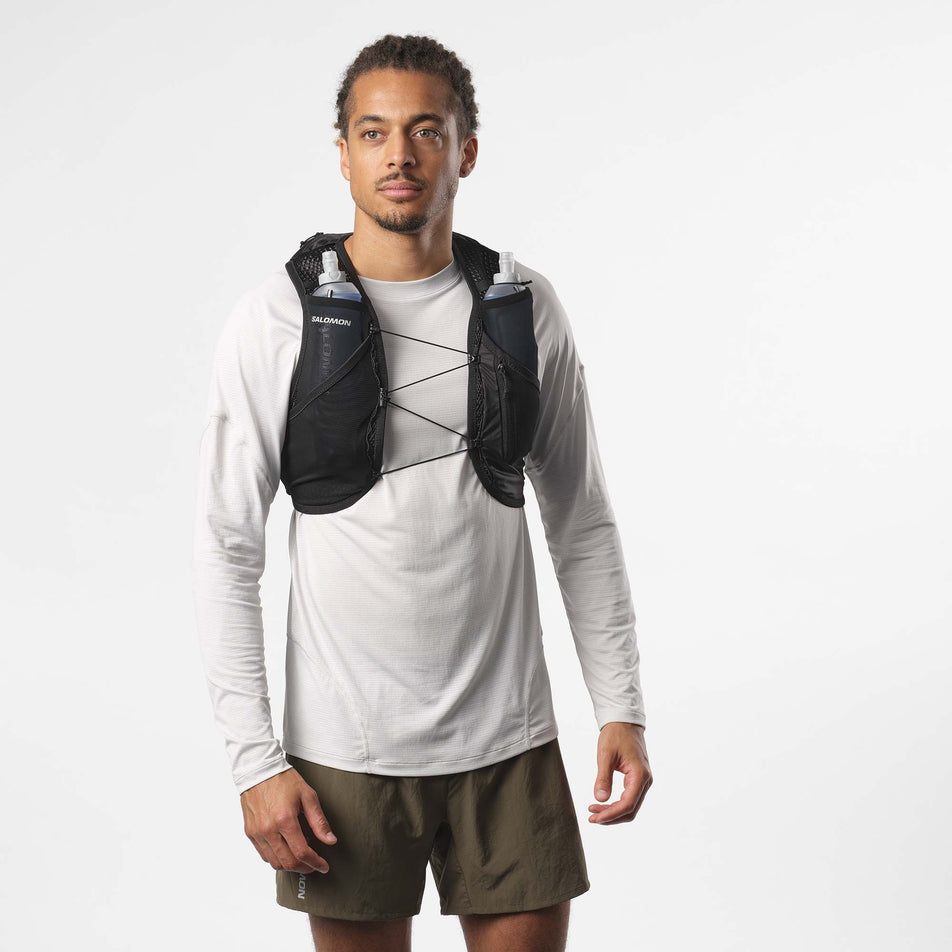 Front view of a model wearing a Salomon Unisex Active Skin 8 Running Vest with flasks. Black/Metal colourway. Model is also wearing a running top and shorts. (8151560880290)