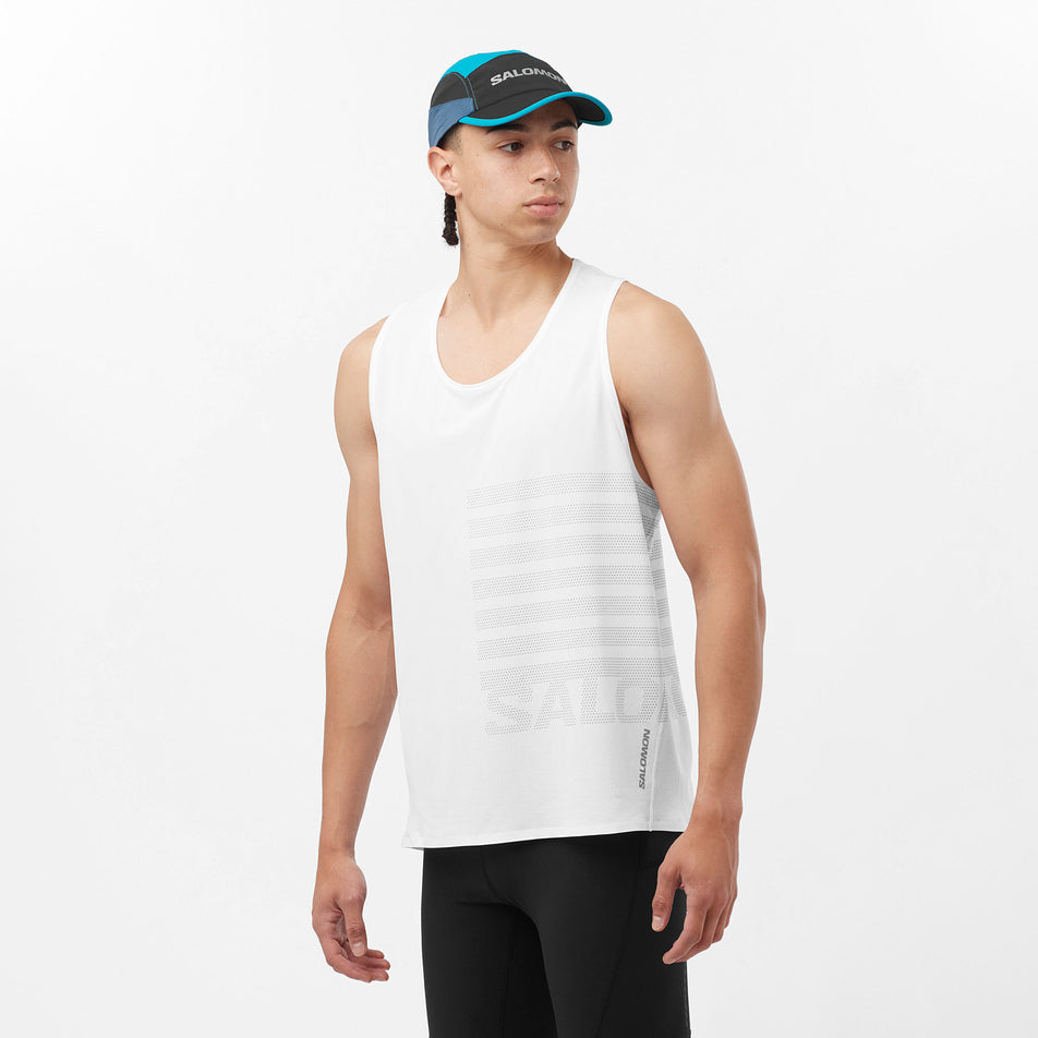 Front view of a model wearing a Salomon Men's Sense Aero GFX Singlet in the White/Peacock Blue colourway. Model is also wearing a Salomon cap and leggings. (8311799152802)