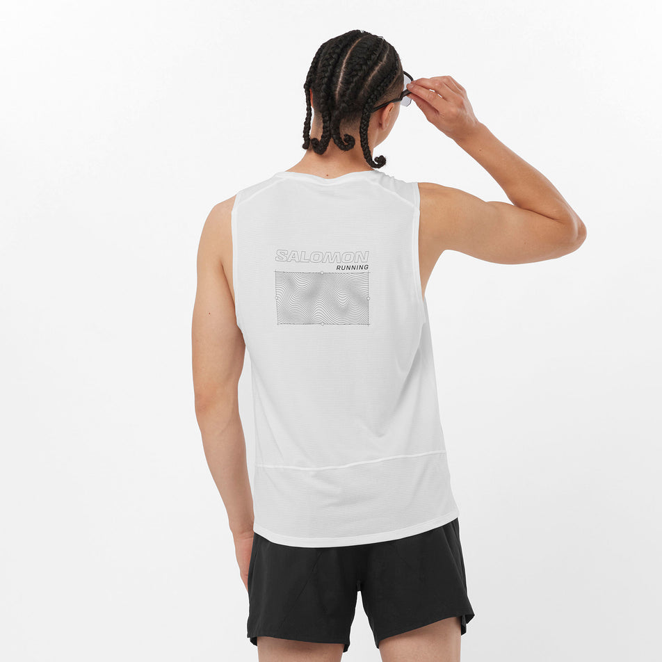Back view of a model wearing a Salomon Men's Cross Run Tank GFX in the White colourway. Model is also wearing sunglasses and shorts. (8246399729826)