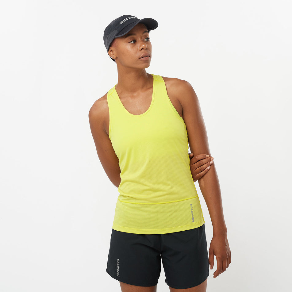 Front view of a model wearing a Salomon Women's Cross Run Tank in the Sulphur Spring colourway. Model is also wearing a Salomon cap and shorts. (8311902896290)