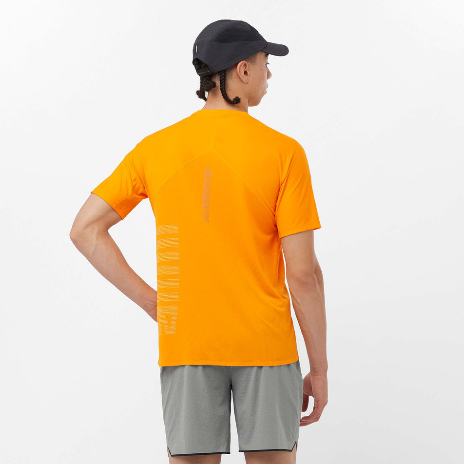 Back view of a model wearing a Salomon Men's Sense Aero GFX Short Sleeve T-Shirt in the Zinnia/White colourway. Model is also wearing Salomon shorts and a Salomon cap. (8157825826978)