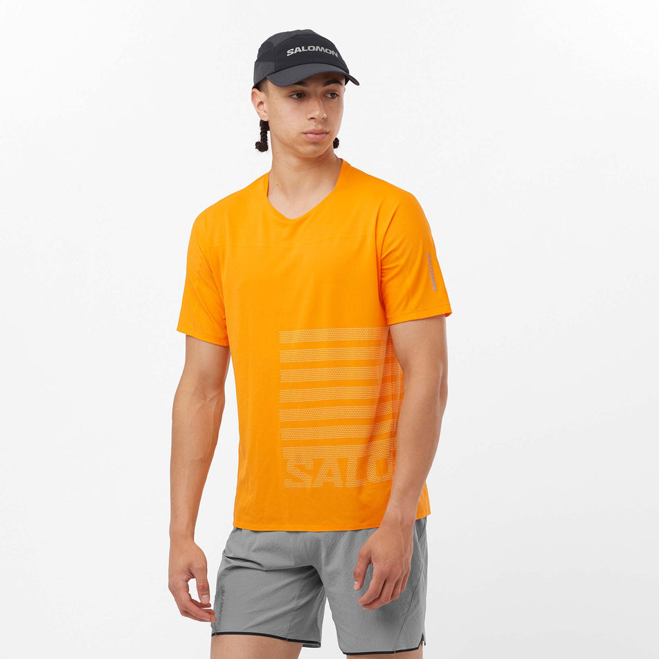 Front view of a model wearing a Salomon Men's Sense Aero GFX Short Sleeve T-Shirt in the Zinnia/White colourway. Model is also wearing Salomon shorts and a Salomon cap. (8157825826978)