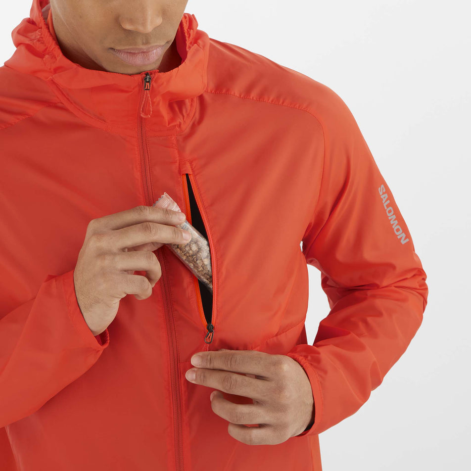 A model demonstrating that nutrition can be stored in the chest pocket of a Salomon Men's Bonatti Cross Wind Jacket Hoodie. Jacket is being worn by a model.  (8466593087650)