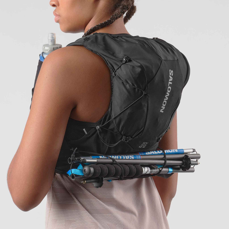 A model demonstrating running poles stowed in the Salomon Women's ADV Skin 12 Set Running Vest in the Black/Asphalt colourway.