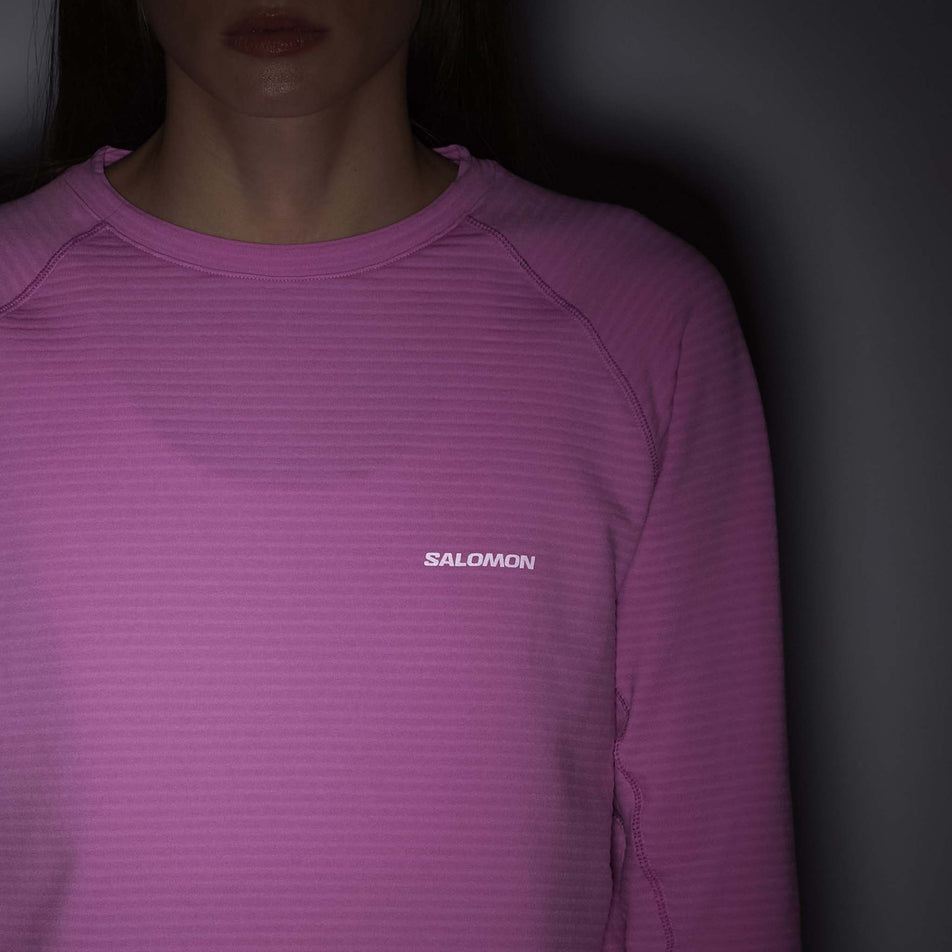 The reflective logo on the front of the Salomon Women's Essential Lightwarm Long-Sleeve Baselayer in the Cyclamen colourway. (8726946578594)
