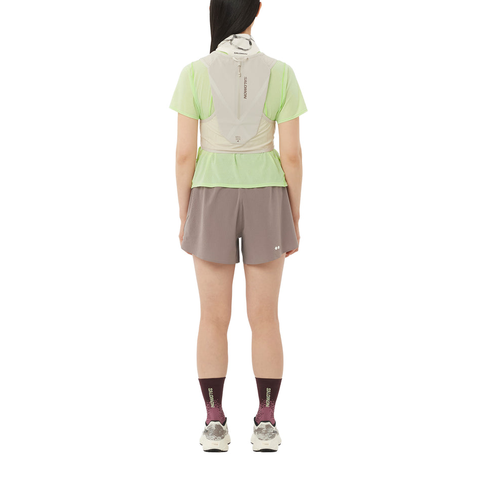 Back view of a model wearing the Salomon Women's SHKout Air Cropped Short-Sleeve T-Shirt in the Butterfly colourway with a hydration vest.
