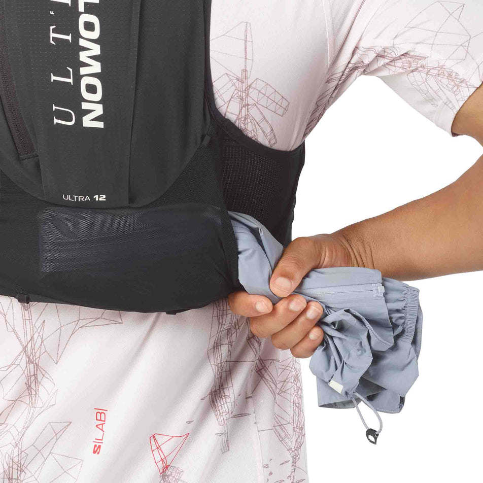 A model demonstrating the back stash pocket on the Salomon Unisex S/LAB Ultra 12 Running Vest in the Black colourway.