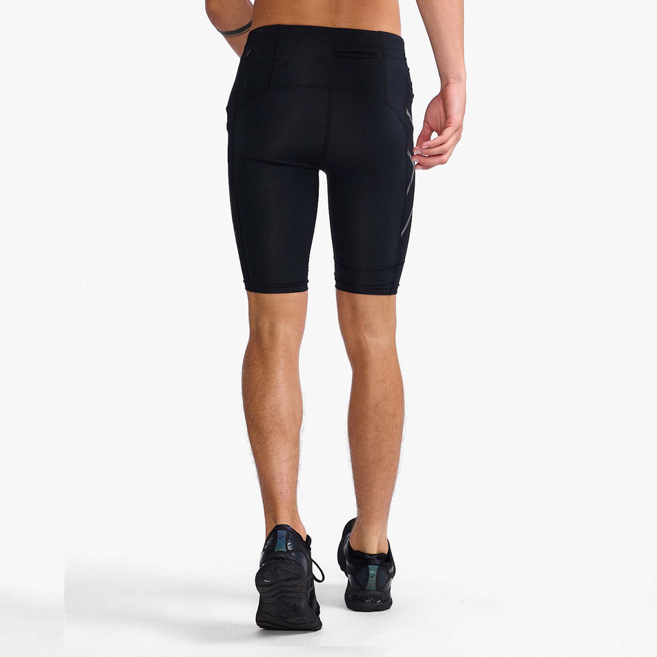Back view of a model wearing a pair of 2XU Men's Light Speed Compression Shorts in the Black/Black Reflective colourway. Model is also wearing a pair of running shoes. (8108354699426)