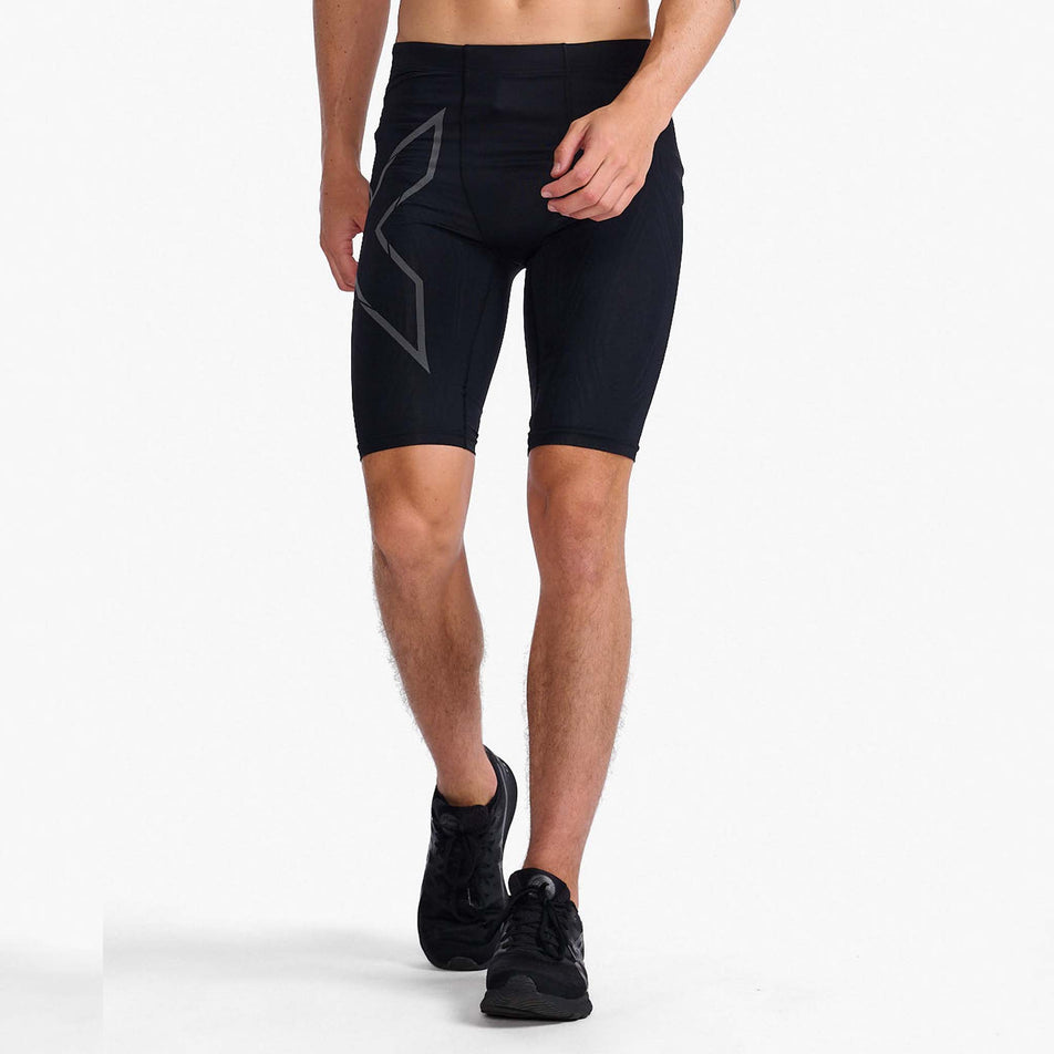 Front view of a model wearing a pair of 2XU Men's Light Speed Compression Shorts in the Black/Black Reflective colourway. Model is also wearing a pair of running shoes.  (8108354699426)
