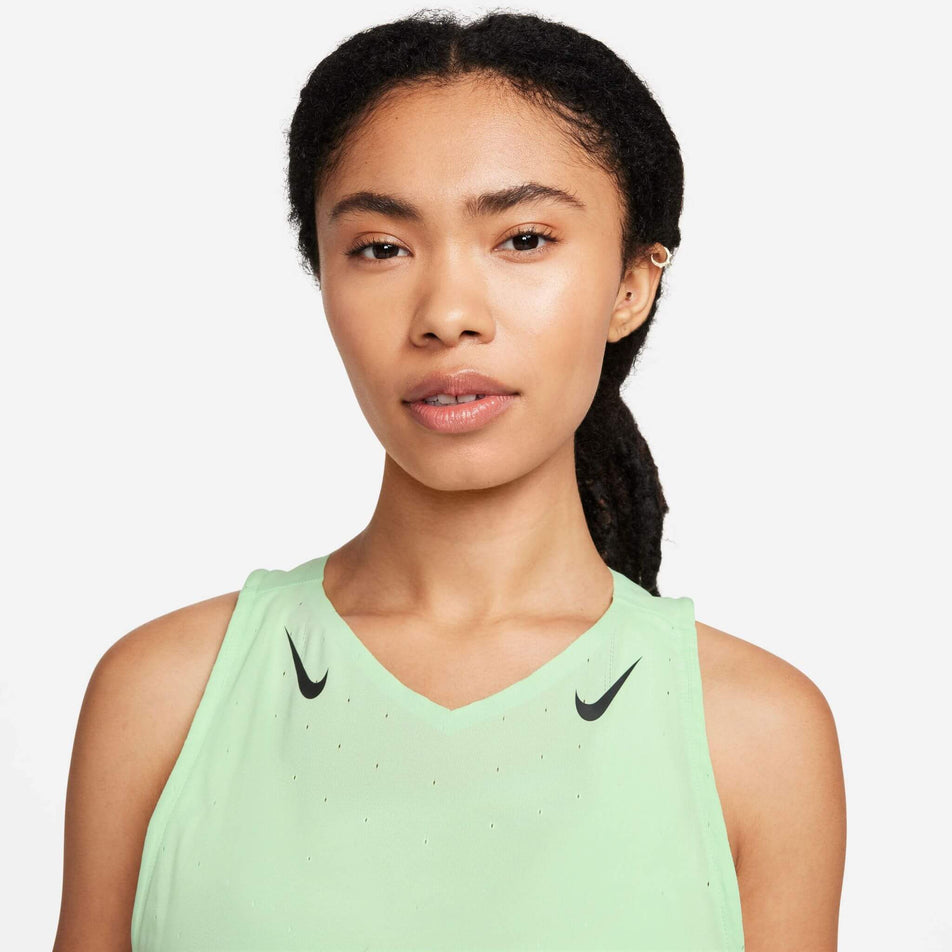 Close-up front view of a model wearing the Women's AeroSwift Dri-FIT ADV Running Singlet in the Vapor Green/Black colourway. Only the upper section of the top can be seen in the image. (8186003357858)