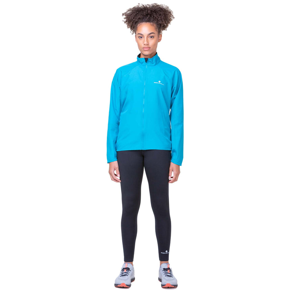 Front view of a model wearing a Ronhill Women's Core Jacket in the Azure/Bright White colourway. Model is also wearing Ronhill running leggings and Altra running shoes. (8159243108514)