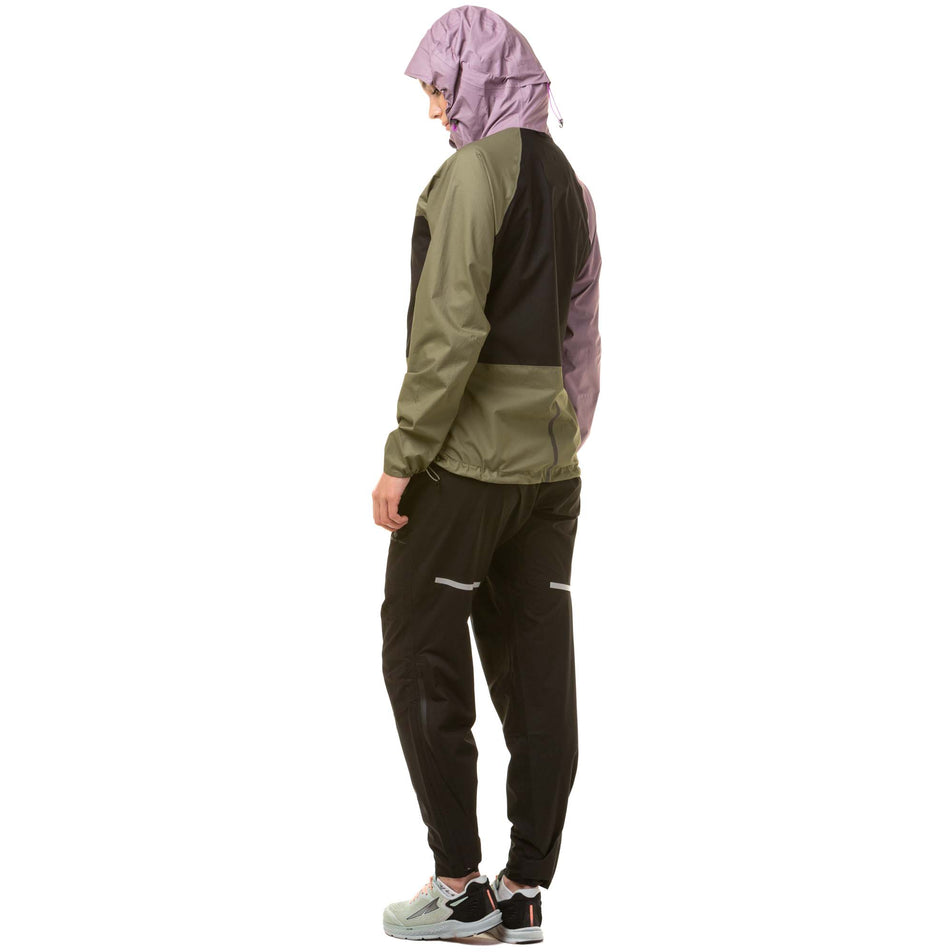 Back view of a model wearing a Ronhill Women's Tech Fortify Jacket in the Woodland/Stardust/Black, with the hood up. Model is also wearing black running trousers and grey running shoes. (8024348328098)
