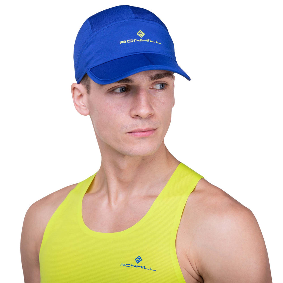 Front view of a model wearing a Ronhill Unisex Air-Lite Split Cap in the Ocean/Citrus colourway. Model is also wearing a Ronhill vest. (8160950223010)