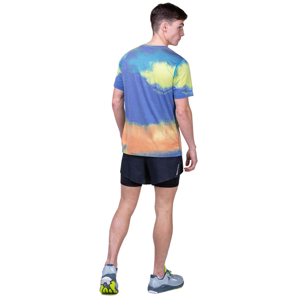 Back view of a model wearing a Ronhill Men's Tech Golden Hour Tee in the Multi Rave colourway. Model is also wearing Ronhill running shorts and Altra running shoes. (8160879149218)