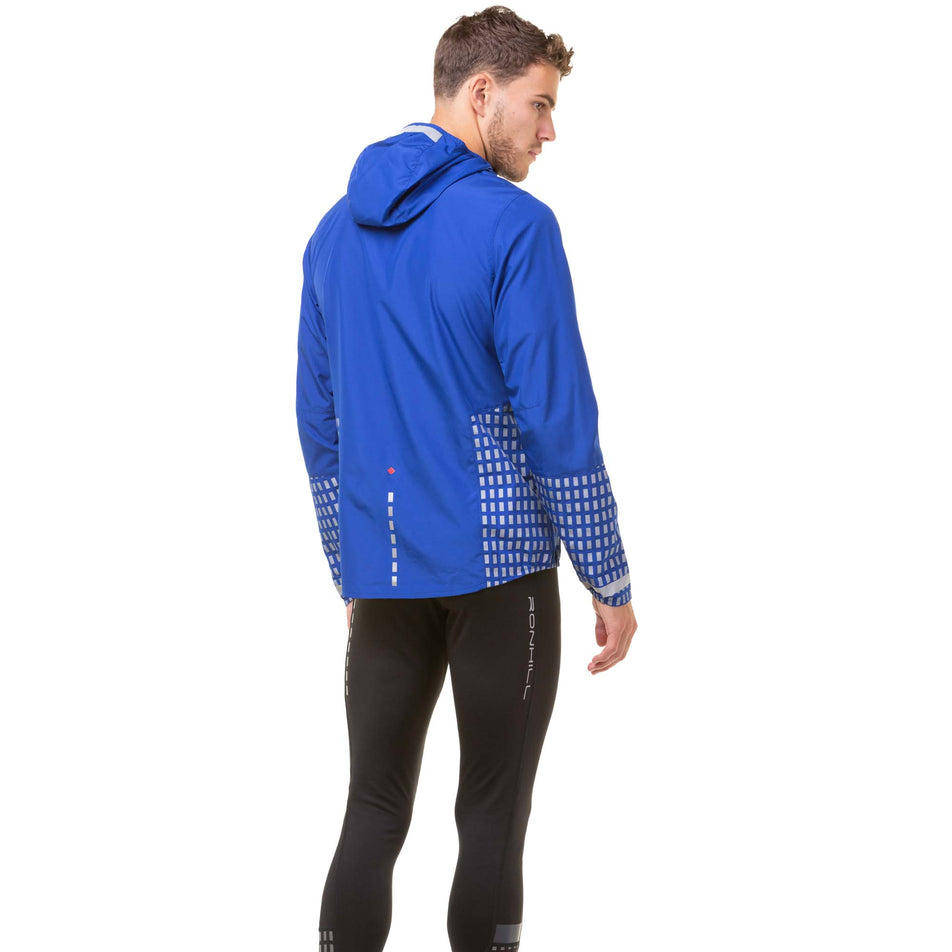 Back view of a model wearing a Ronhill Men's Tech Afterhours Jacket in the Cobalt/Flame/Reflect colourway. Model is also wearing black Ronhill running tights. (8032156385442)