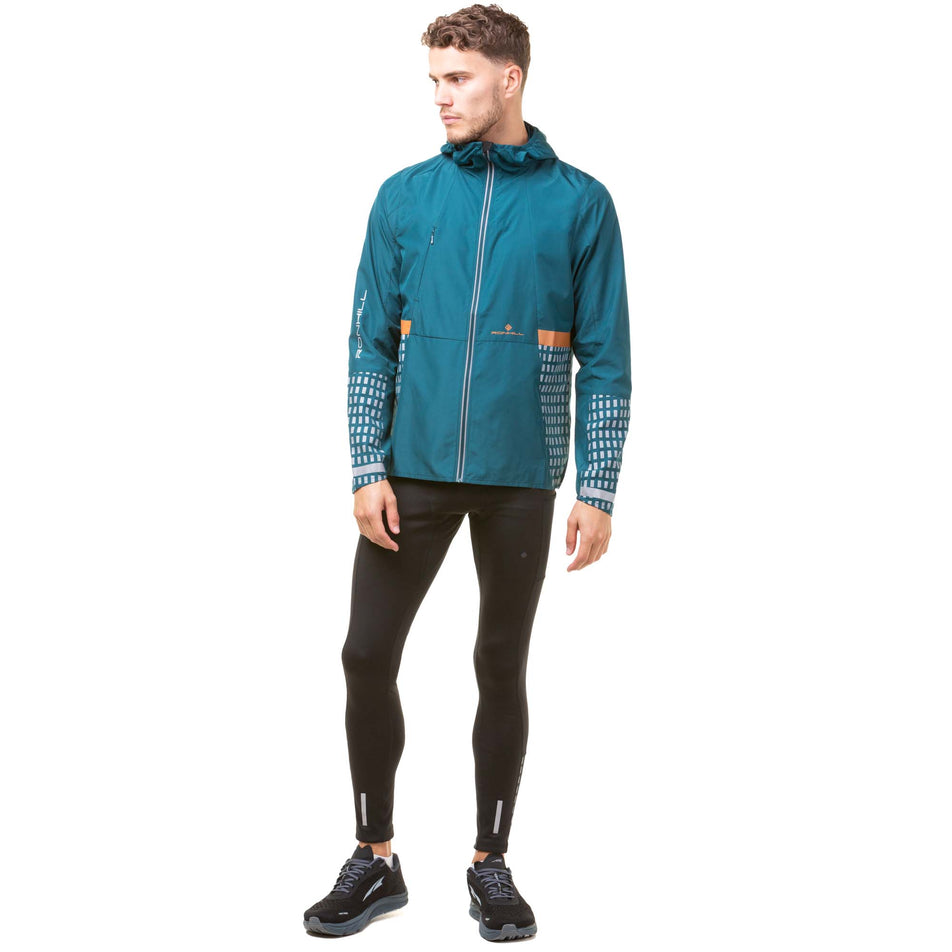 Front view of a model wearing a Ronhill Men's Tech Afterhours Jacket in the Deep Lagoon/Copper Reflect colourway. Model is also wearing Ronhill running tights and Altra running shoes. (8047865364642)