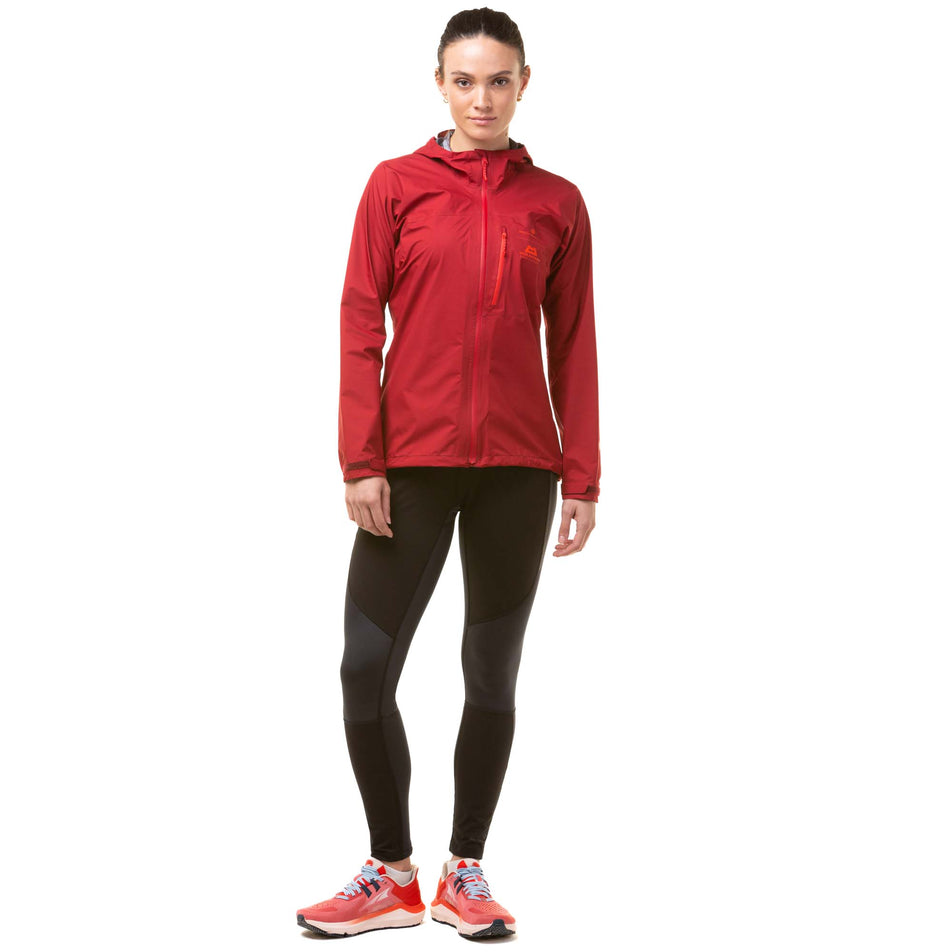 Front view of a model wearing a Ronhill Women's Tech GORE-TEX Mercurial Jacket in the Jame/Flame colourway. Model is also wearing black Ronhill running leggings and red Altra running shoes. (8047328034978)