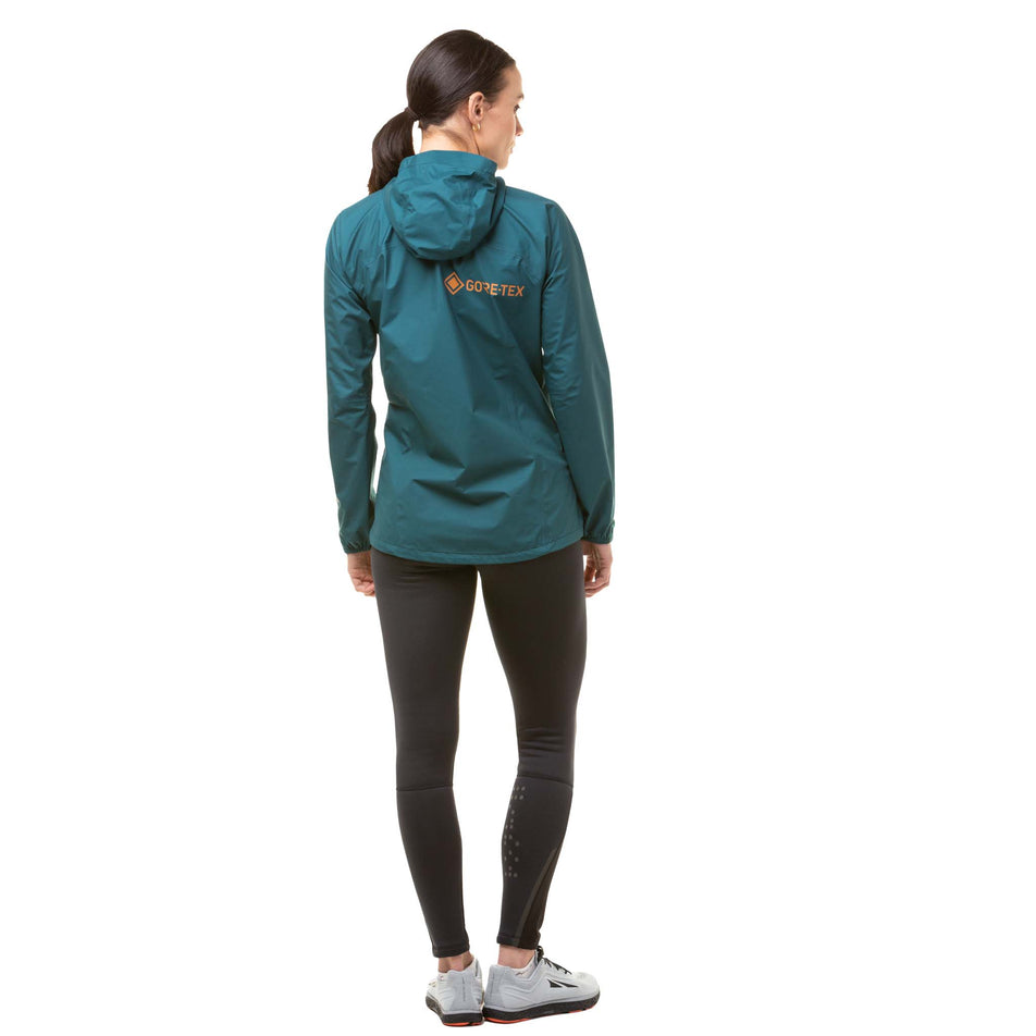 Back view of a model wearing a Ronhill Women's Tech Gore-Tex Mercurial Jacket in the Deep Lagoon/Copper colourway. Model is also wearing Ronhill running leggings and Altra shoes. (8059839119522)