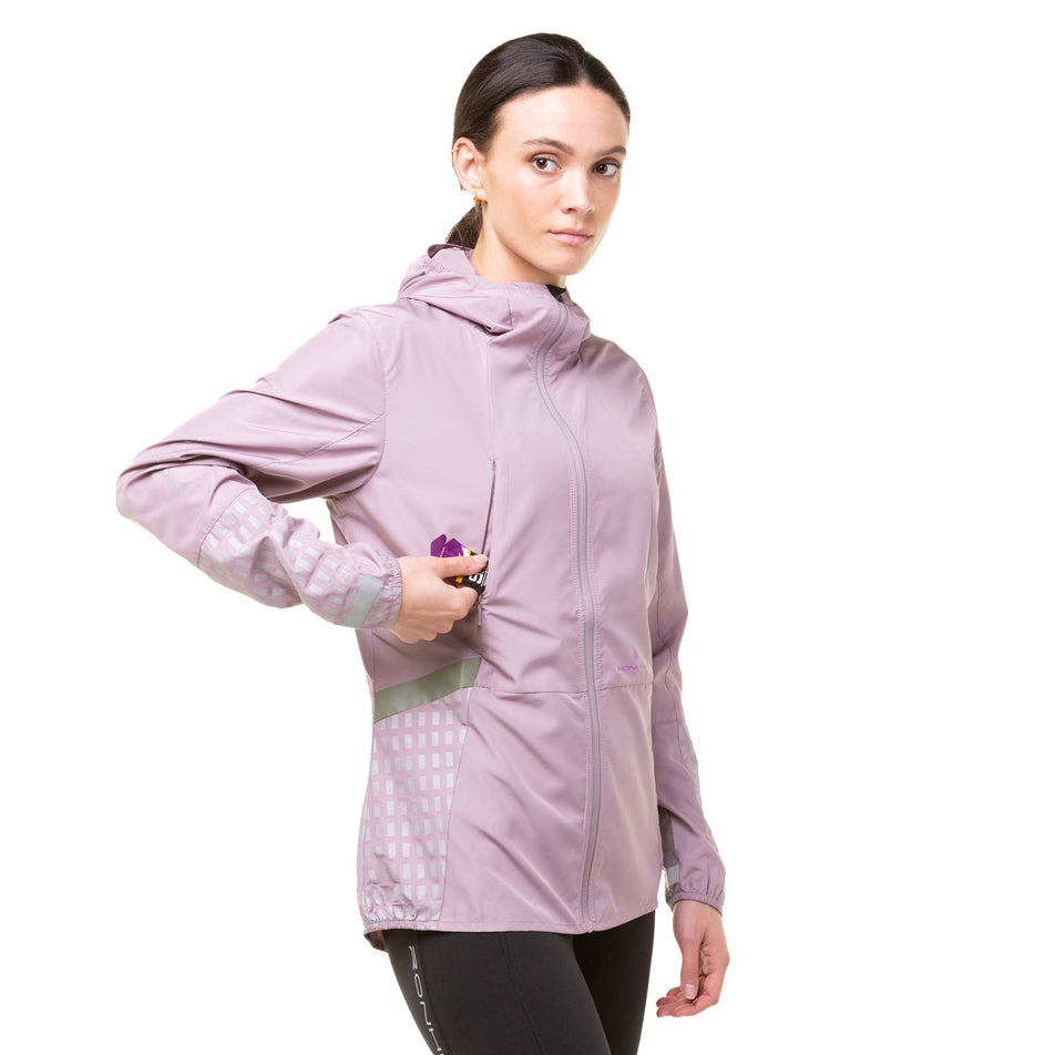 Front view of a model wearing a Ronhill Women's Tech Afterhours Jacket in the Stardust/Thistle/Reflect colourway. Demonstrating that an energy gel can be stored in the front-right pocket.  (8019199557794)