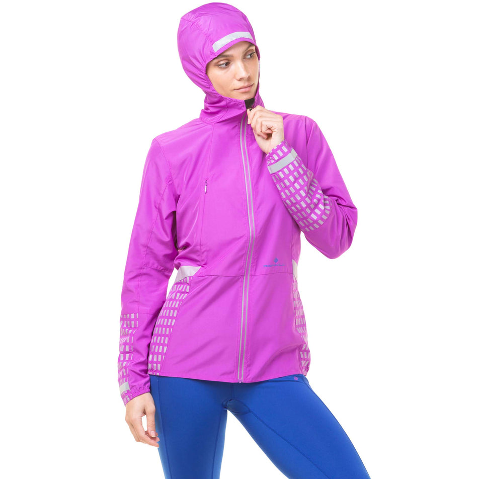Front view of model wearing a Ronhill Women's Tech Afterhours Jacket in the Thistle/Cobalt/Reflect colourway. Model is wearing the jacket with the hood up. (8047250374818)