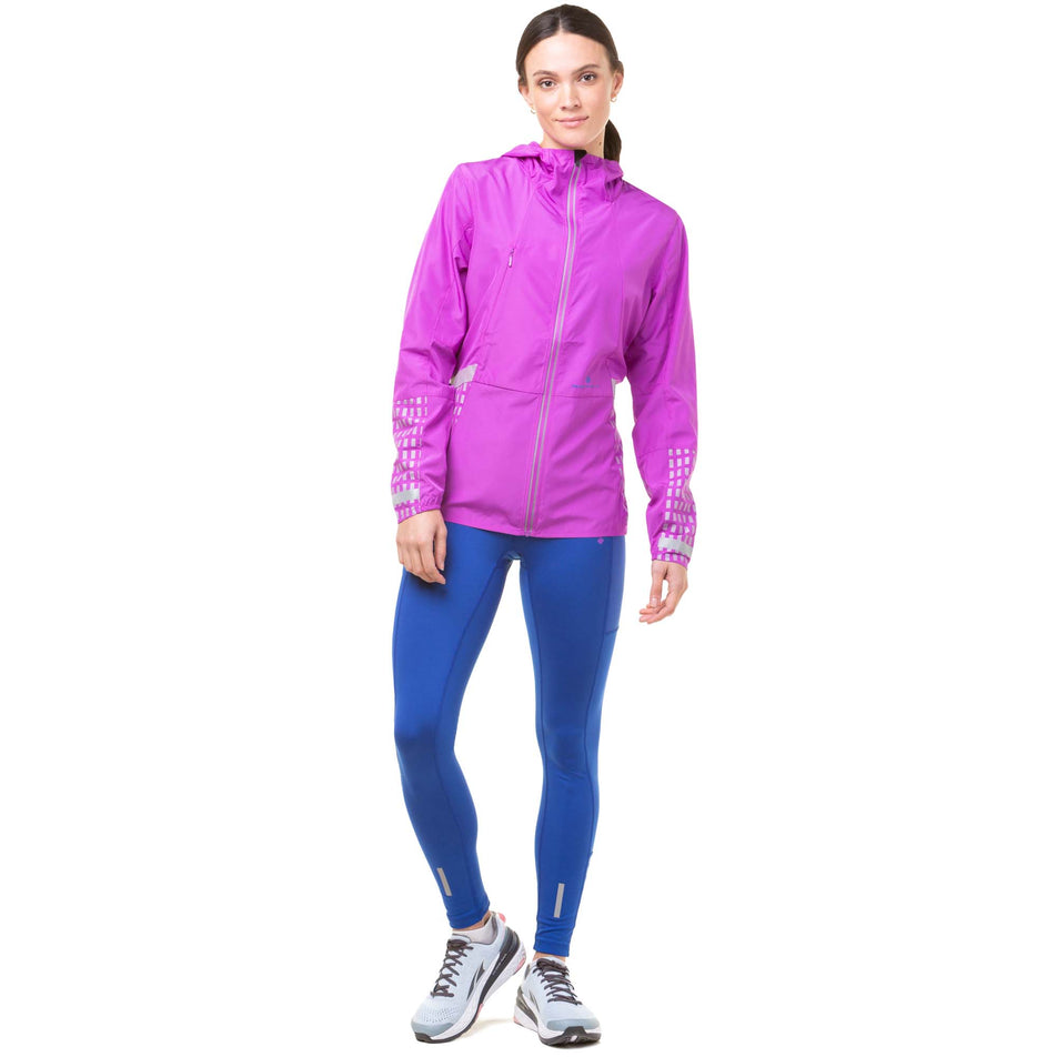 Front view of model wearing a Ronhill Women's Tech Afterhours Jacket in the Thistle/Cobalt/Reflect colourway. Model is also wearing blue Ronhill leggings and Altra running shoes. (8047250374818)