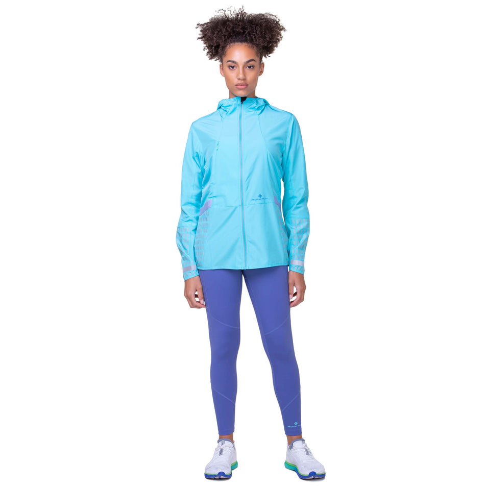 Front view of a model wearing the Ronhill Women's Tech Afterhours Jacket in the Aquamint/Reflect colourway. Model is also wearing Ronhill leggings and Altra running shoes.  (8160853983394)
