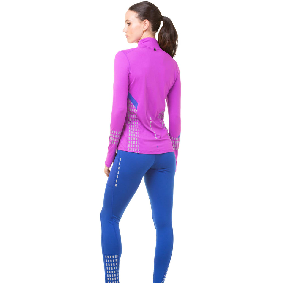 Back view of a model wearing a pair of Ronhill Women's Tech Afterhours Tights in the Cobalt/Thistle/Reflect colourway. Model us also wearing a purple Ronhill running top. (8047316861090)