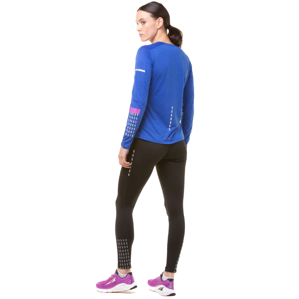 Back view of a model wearing a Ronhill Women's Tech Afterhours L/S Tee in the Cobalt/Thistle/Reflect colourway. Model is also wearing black Ronhill running leggings and purple Altra running shoes. (8047287500962)