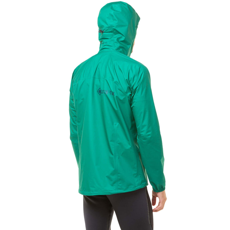 Back view of a model wearing a Men's Tech GORE-TEX Mercurial Jacket in the Lawn/Deep Lagoon colourway. Model is wearing the jacket with the hood up. (8048099786914)