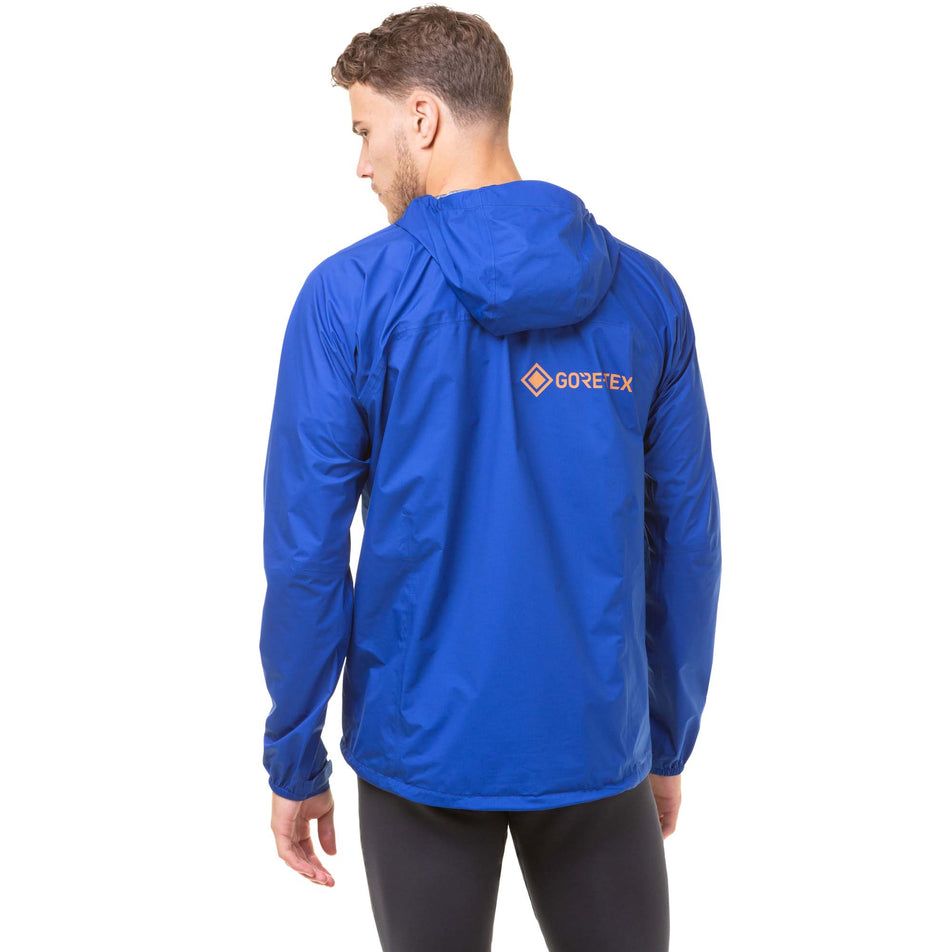 Back view of a model wearing a Ronhill Men's Tech Gore-Tex Mercurial Jacket in the Cobalt/Copper colourway. Model is also wearing black Ronhill running tights. (8032222019746)