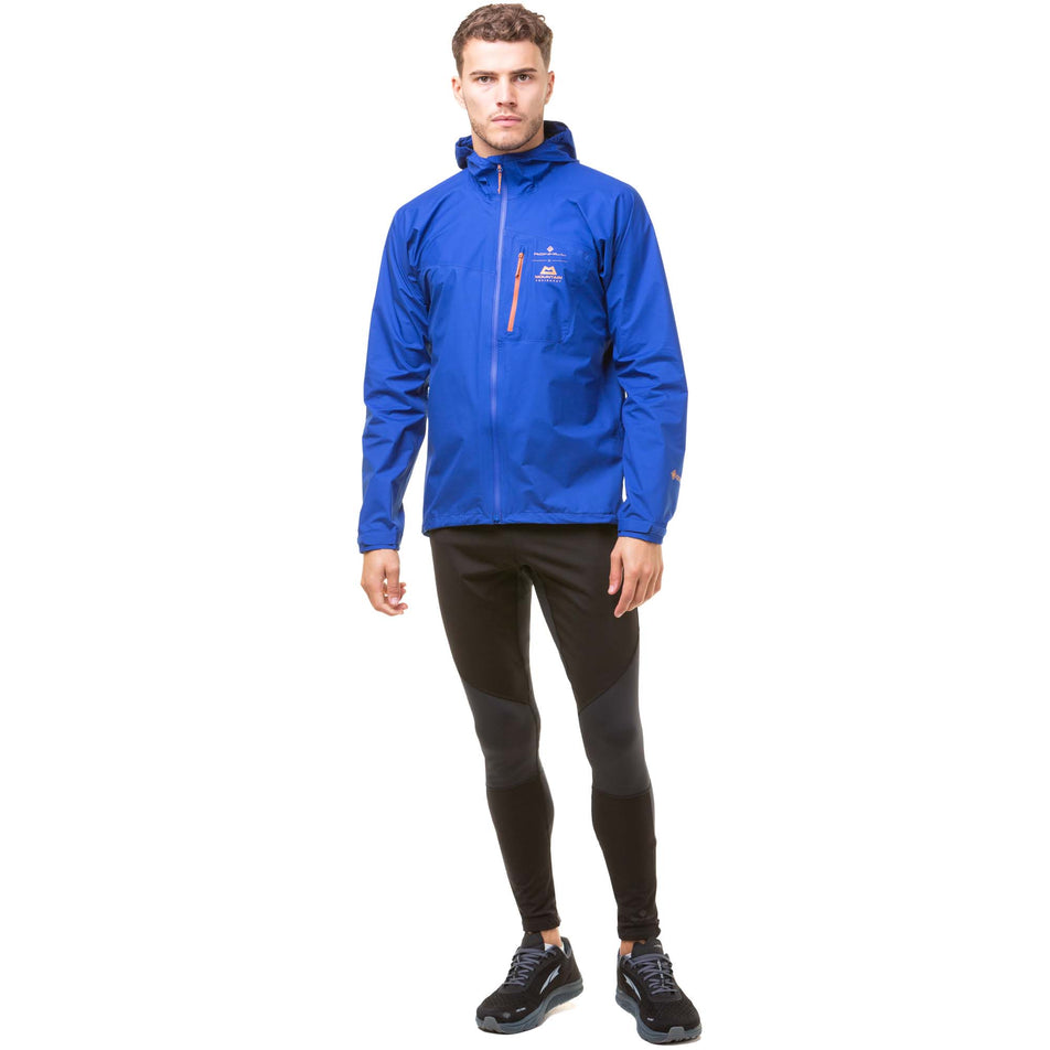 Front view of a model wearing a Ronhill Men's Tech Gore-Tex Mercurial Jacket in the Cobalt/Copper colourway. Model is also wearing black Ronhill running tights and black Altra running shoes. (8032222019746)
