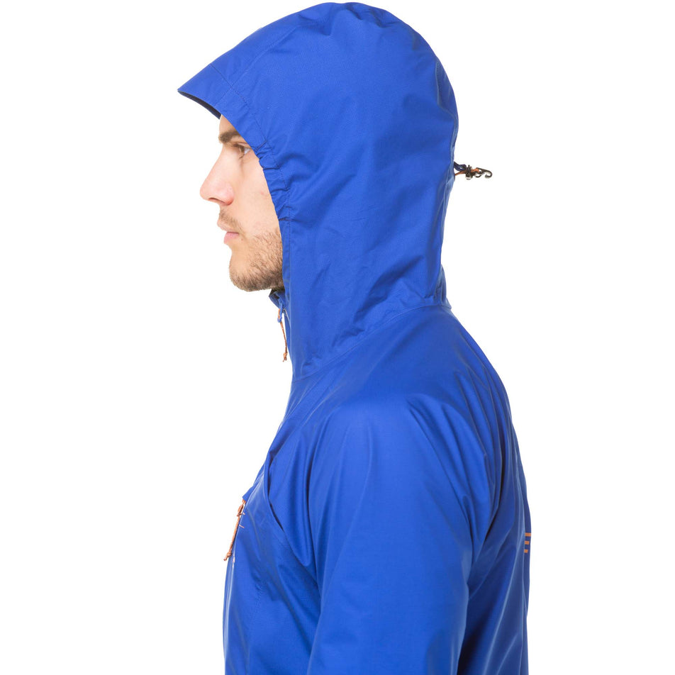 Close-up side view of a model wearing a Ronhill Men's Tech Gore-Tex Mercurial Jacket in the Cobalt/Copper colourway. Model is wearing the jacket with the hood up. Upper half of jacket can be seen in the image. (8032222019746)