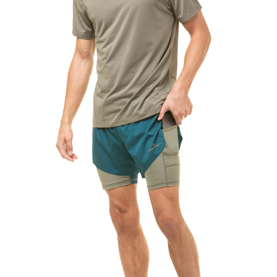 A model demonstrating that a phone can be stored in the stretch pocket - located on the outside of the left-thigh on a pair of Ronhill Men's Tech Distance Twin Shorts. (8048123084962)